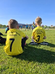 Zwei Kinder im Rugbytrikot schauen anderen bei einer Trainingseinheit zu