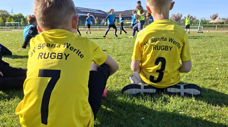 Zwei Kinder im Rugbytrikot schauen anderen bei einer Trainingseinheit zu